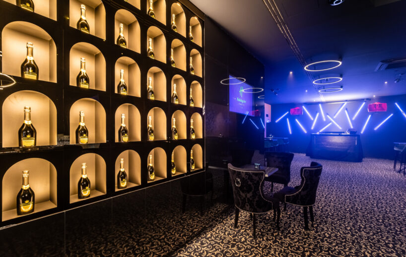 Pódium HI.5 Night Bar a osvetlená stena s fľašami.
