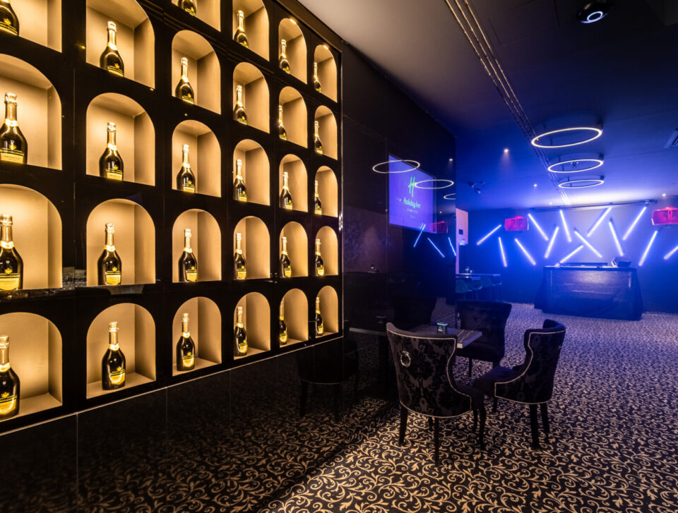 Pódium HI.5 Night Bar a osvetlená stena s fľašami.